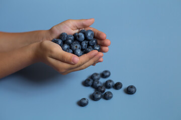 kid's hands with vitamin blueberries on the blue background