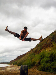 A young guy on the beach does an acrobatic stunt in the air on a twine	
