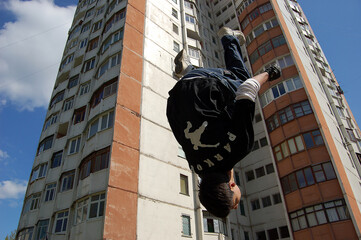 a guy does a backflip off a wall in parkour style against the backdrop of a high-rise building	
