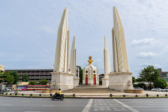 A motorcycle, bus and car traffic pass Democracy Monument in Bangkok
