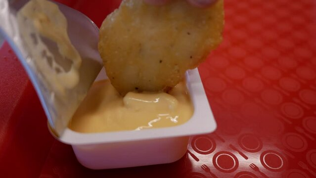 Girl is immersing a crispy naggets into a delightful yellow cheese sauce. The girl eats delicious fast food