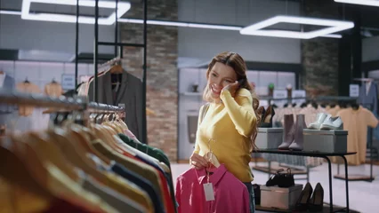 Fotobehang Excited shopaholic calling smartphone choosing clothes in shop mall closeup © stockbusters