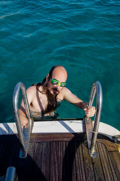Man with googles coming on a boat after swimming in the sea