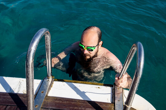 Man with googles coming on a boat after swimming in the sea