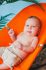 A small newborn boy is sitting in a baby chair. Children's chair chaise longue.