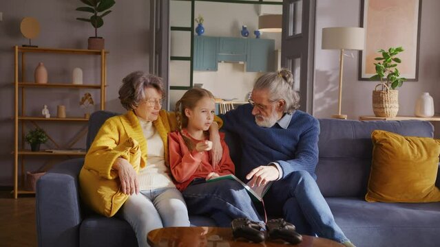 Cute girl sitting between grandparents and holding book