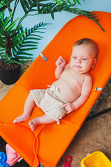 A small newborn boy is sitting in a baby chair. Children's chair chaise longue.