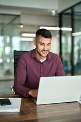 Busy smiling professional business man company employee, young male worker software developer, latin businessman typing on computer using laptop working with online data at office desk. Vertical.