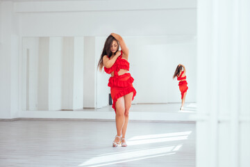 Graceful woman dressed in red Latin dancing dress doing elegant dance pas in white color big hall...