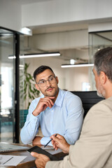 Fototapeta premium Busy executive team of two business men discussing digital finance banking project strategy working in office with laptop and tablet. Financial advisor consulting partner at meeting. Vertical