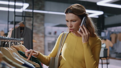 Nervous shopping woman calling mobile phone at expensive clothing store closeup