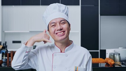 Close Up Of Asian Man Chef Smiling And Making Call Me Gesture To Camera While Standing In Home Kitchen