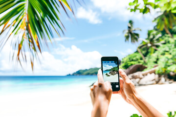 Close-up of a person holding a phone taking a picture of a beautiful tropical beach