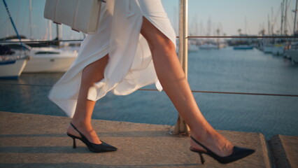 Girl feet strolling quay in trendy high-heels close up. Stylish woman walking