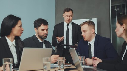 Group of businessmen in meeting, one man holding tablet and others engaged in discussion. Business team applauds colleague following successful presentation