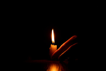 Women's hands near a candle flame in the dark, faith and religion