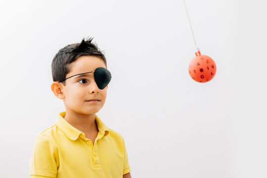 Boy wearing medical eye patch looking at therapy ball