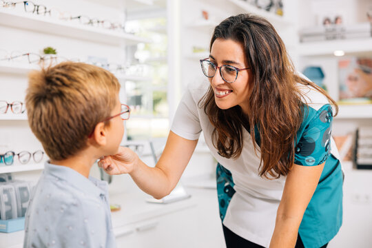 Cheerful optician helping boy to choose glasses at work