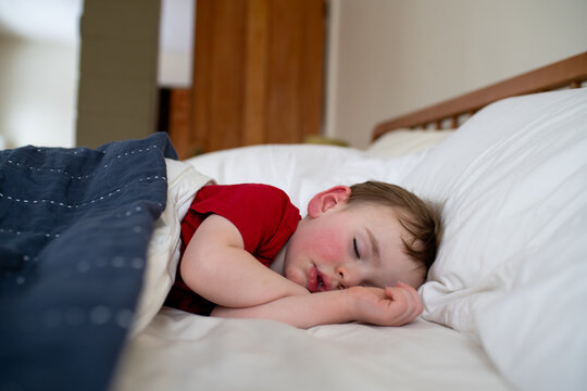 Sleeping Toddler Naps Peacefully with Hands by Face in Bed at Home