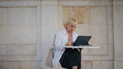 Retired manager working remotely at street cafe. Mature woman typing laptop