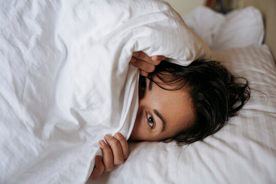 A woman in bed hides her face under the blanket