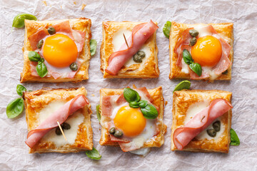 Puff pastry mini tarts with egg and ham on a white  background, top view. Delicious breakfast or Easter snack - 759167030