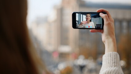 Street girl video calling friend closeup. Smiling woman waving smartphone screen