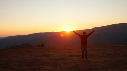 Man with raised arms in the mountains at sunset. Copy space.