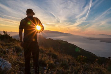 Hiker man with scenic sunrise view from top of mount Kula near Omis, Dinara mountains, Split-Dalmatia, Croatia, Europe. Coastline of Makarska Riviera, Adriatic Sea. Balkans in summer. Biokovo mountain