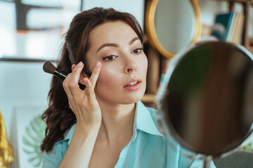 Young pretty woman does makeup at home while looking in the mirror
