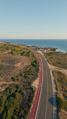 Scenic road running seaside under blue sky aerial view. Straight asphalt highway