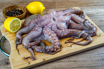 Raw octopus with lemon on a wooden board. 
