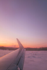 Fototapeta premium Orange sunset landscape on a snowy ground road while an airplane landing