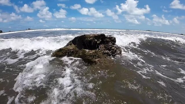 A serene coastal view - White waves slowly wash over and lap around a rock in slow motion. With clouds in the background. copy space