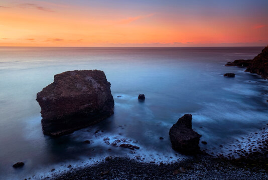 Playa del Bollullo unique sea stacks stand sentinel under a pastel twilight sky, with waves gently lapping the pebbled shore
