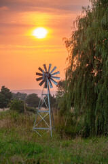A windmill beside a willow tree during a stunning sunset in the summer