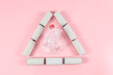 Toilet paper rolls are arranged in a triangle with a crumpled bottle on pink.