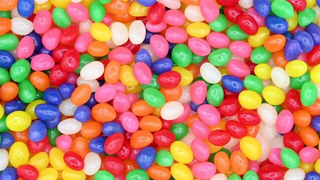 4K HD video of background of bright vibrant colorful jelly beans, wood spoon comes in and scoops up some candy.
