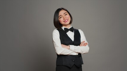 Asian receptionist posing with arms crossed on camera, feeling confident and professional in a formal suit and tie. Woman with front desk staff occupation, greeting guests in studio. Camera A. - obrazy, fototapety, plakaty