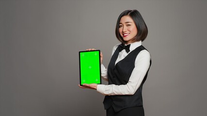 Woman concierge presenting greenscreen display on tablet, showing chromakey template on screen....