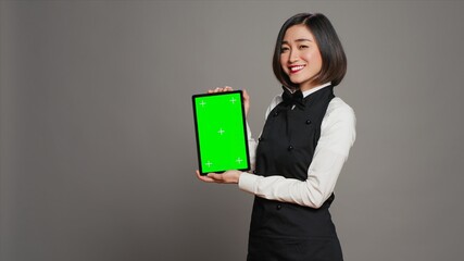 Asian restaurant hostess showing greenscreen display in studio, presenting isolated mockup layout...