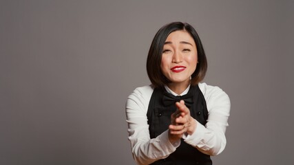 Restaurant hostess clapping hands and celebrating for someone, cheering and saying congratulations in studio. Asian waitress with uniform and apron applauding a person, acclaim. Camera B.
