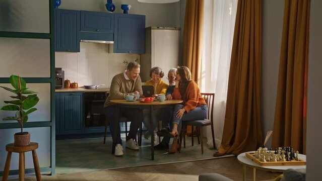 Parents sitting with adult offsprings by kitchen table