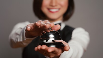 Receptionist posing with service bell and ringing it on camera, expressing assistance from front...