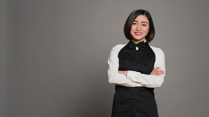 Restaurant hostess posing with confidence in studio, standing with arms crossed over grey...