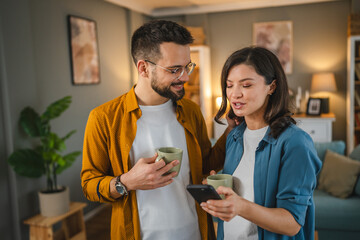 Adult couple man and woman husband wife have a cup of coffee use mobile phone search internet social network happy smile