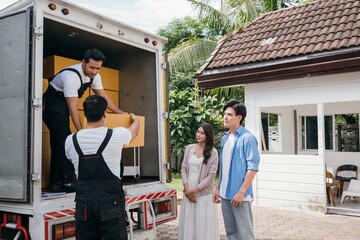 A couple receives professional assistance in moving to their new house. The teamwork of employees is evident as they unload and lift cardboard boxes during the relocation. Moving Day Concept