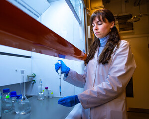 A female scientist and chemist pipetting samples into a test tube under fume hood in a chemical laboratory, focused on precision and research