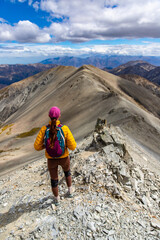 woman walking down a steep rocky mountain ridge of castle hill peak, canterbury, new zealand soth...