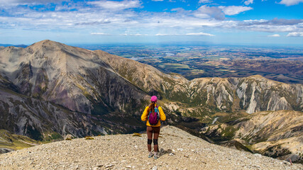 Fototapeta premium hiker girl walking alongside the ridge between castle hill peak and foggy peak near porters pass in torlesse tussocklands national park, canterbury, new zealand south island; southern alps